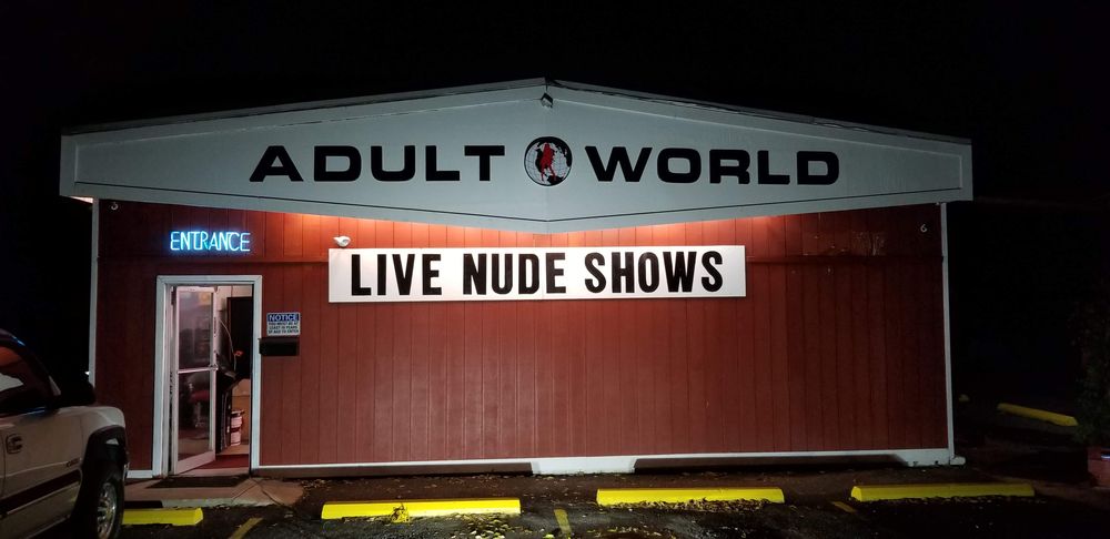 Adult World storefront at night, lit up with the Adult World sign and a Live Nude Shows marquee